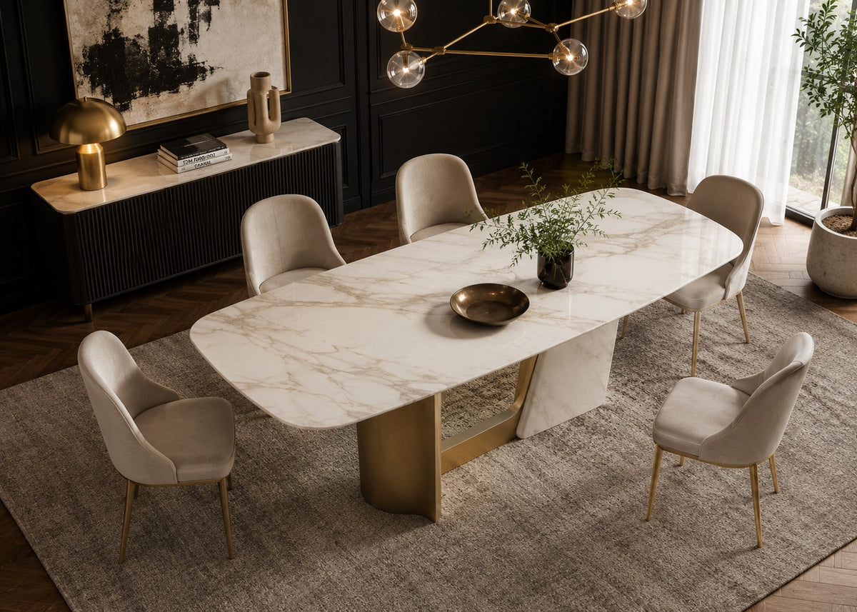 A modern dining room scene featuring a rectangular white marble dining table with a gold metal pedestal base, surrounded by six beige upholstered chairs on a textured gray rug.