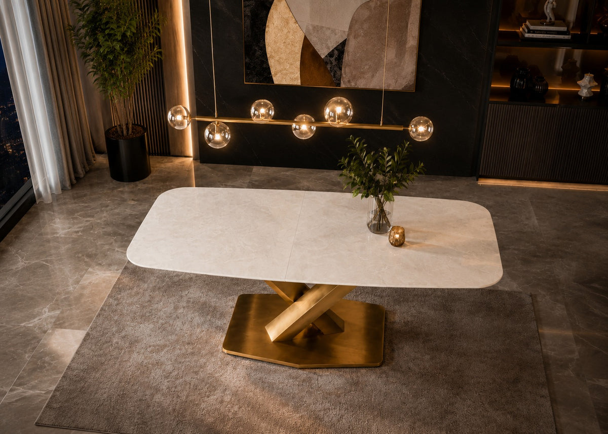A modern rectangular dining table with a white marble-look top and a polished gold-tone geometric metal base, styled in a contemporary dining room setting.