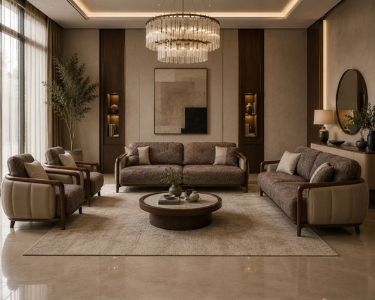 A luxury modern living room featuring a coordinated furniture set including a brown textured sofa, two matching armchairs, a round dark wood coffee table, and a large beige area rug. The room is decorated with a tiered crystal chandelier, warm wall sconces, and a large abstract painting.