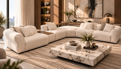 A modern U-shaped sectional sofa in warm off-white upholstery, styled in a luxurious, sunlit living room with a marble coffee table, textured rug, and warm wood accents.