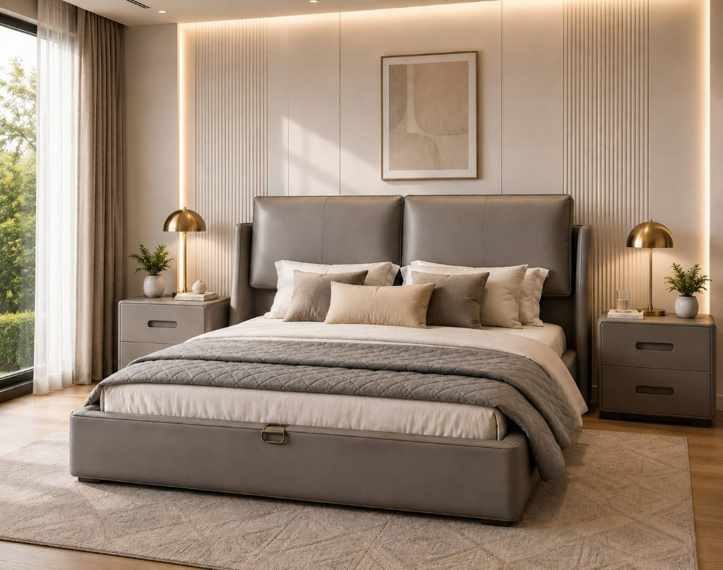 A modern bedroom featuring a large gray upholstered bed with a high padded headboard and matching footboard, styled with neutral bedding and pillows. The room has a textured beige wall with vertical slats, warm ambient lighting, two matching gray nightstands, gold table lamps, and a large window on the left.