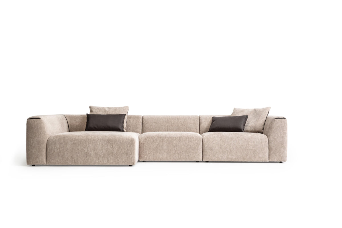 Original Soho L-shape modular sofa front studio view showing left extended chaise, beige textured fabric, two charcoal pillows and broad rounded arms