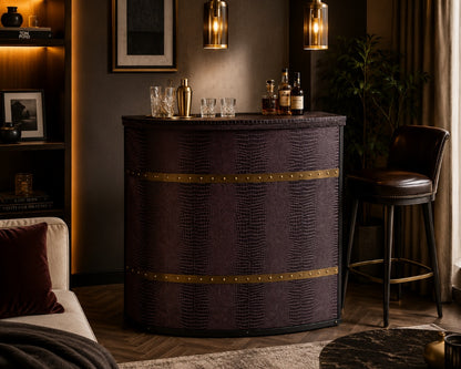 A dark purple faux-croc textured bar cabinet with brass trim, styled in a cozy, dimly lit living room next to a leather bar stool and under warm pendant lights.