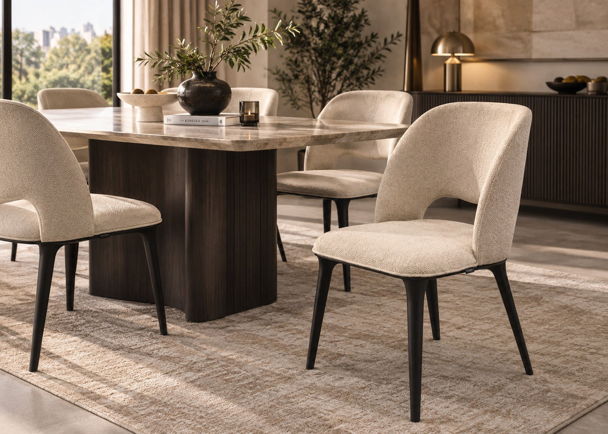 A modern dining room scene featuring a dark wood rectangular table with a light stone top and six upholstered dining chairs in a light beige fabric with dark tapered legs, set on a textured beige rug.
