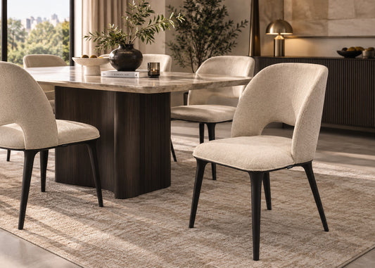 A modern dining room scene featuring a dark wood rectangular table with a light stone top and six upholstered dining chairs in a light beige fabric with dark tapered legs, set on a textured beige rug.