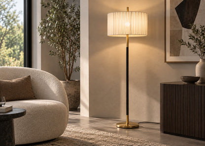 A modern floor lamp with a pleated cream shade, black pole, and gold base, styled in a warm, contemporary living room next to a curved beige sofa and a dark wood sideboard.