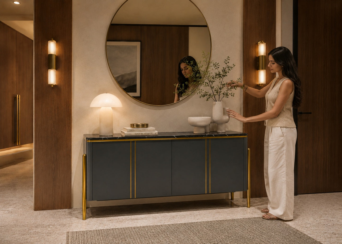 Woman standing in a modern interior space with a round mirror and decorative items.