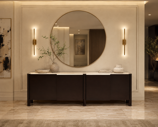 Round mirror on a wall above a dark wooden console table with decorative items.