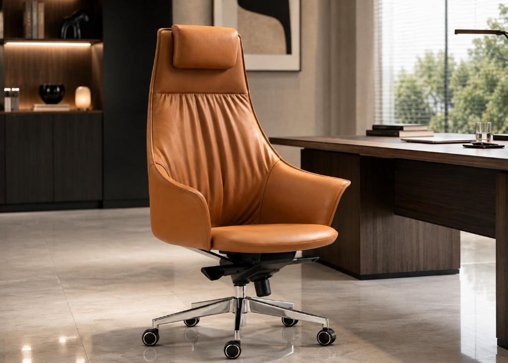 A modern high-back office chair upholstered in tan leather, positioned in a contemporary office setting next to a dark wood desk.