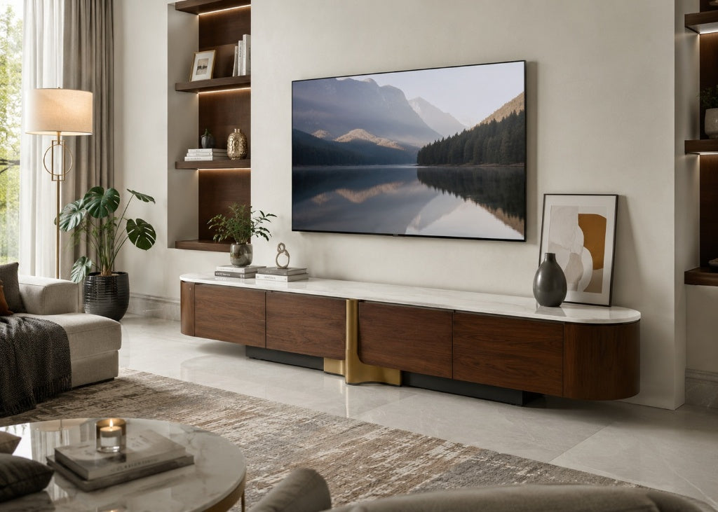 A modern curved media console in dark wood and white with a gold accent leg, styled in a contemporary living room under a large wall-mounted TV displaying a mountain lake scene.
