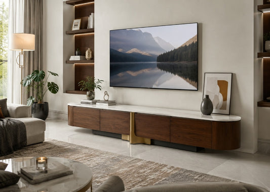 A modern curved media console in dark wood and white with a gold accent leg, styled in a contemporary living room under a large wall-mounted TV displaying a mountain lake scene.