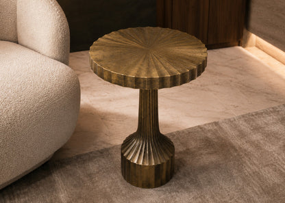 Bronze side table with textured surface next to a beige sofa on a patterned rug.