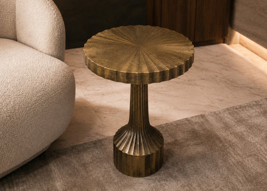 Bronze side table with textured surface next to a beige sofa on a patterned rug.