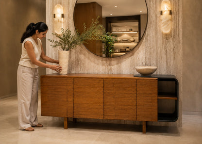 Woman arranging a vase on a wooden sideboard in a modern interior setting.