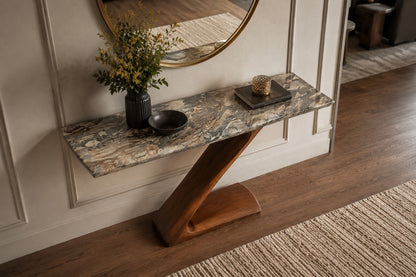 A modern Z-shaped wooden console table with a polished gray and beige marble top, styled in a home entryway with a vase of flowers, a small bowl, and a decorative tray.