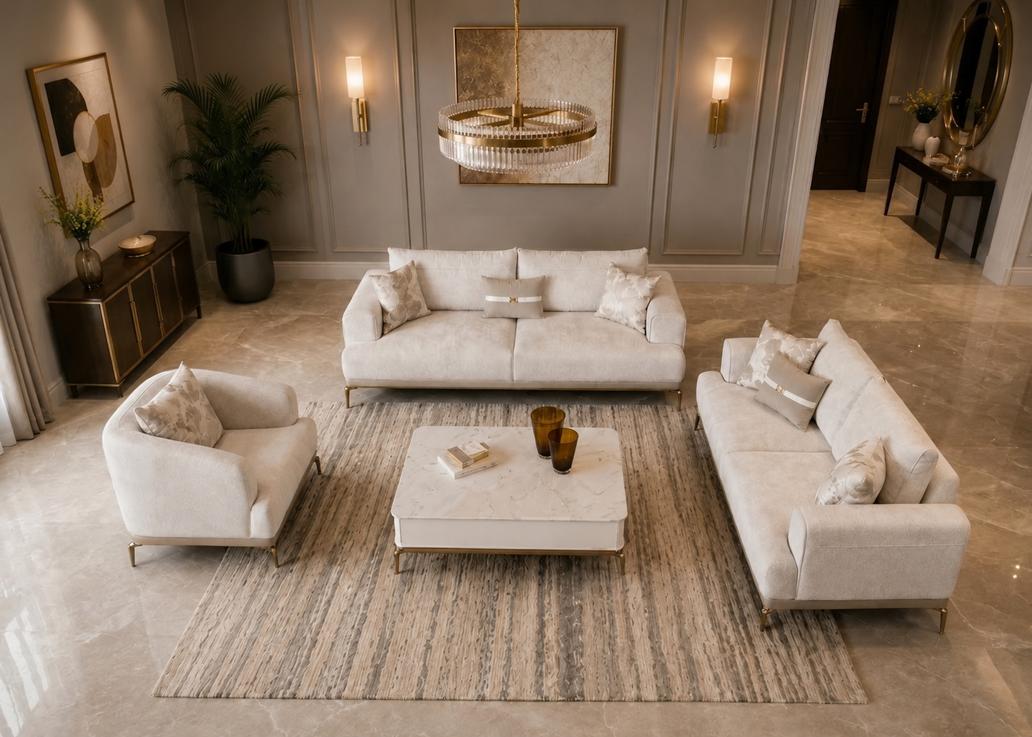 A luxury living room set featuring a cream-colored three-seater sofa, matching two-seater armchair, and a three-seater sofa arranged around a white marble coffee table on a striped area rug. The furniture is set in a high-end modern living room with beige walls, gold sconces, and a crystal chandelier.