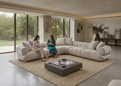 Two women sitting on a large beige sectional sofa in a modern living room with a coffee table and decorative elements.