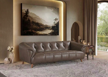 Brown leather sofa in a living room with a painting on the wall and a window in the background.