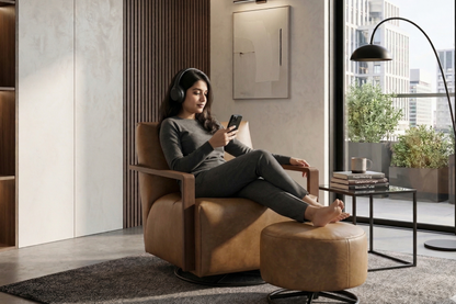 Woman sitting in a brown armchair using a smartphone in a modern living room.