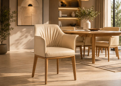 A modern upholstered dining chair in warm cream leather with light wood legs, shown in a sunlit dining room setting.