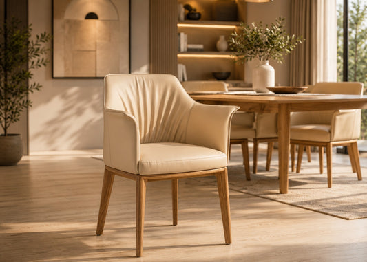 A modern upholstered dining chair in warm cream leather with light wood legs, shown in a sunlit dining room setting.