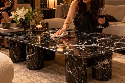 Woman wiping a small wine spill promptly from black marble coffee table with soft cloth, illustrative care scene