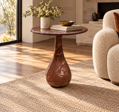Altera burgundy marble side table with elongated round top and single sculptural teardrop pedestal in sunlit luxury room