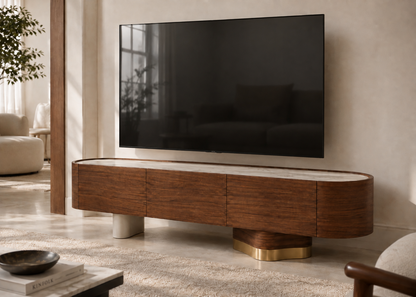 A modern floating TV stand in dark wood with a light stone top and sculptural gold and white legs, holding a large black television in a styled living room.