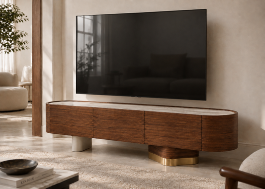 A modern floating TV stand in dark wood with a light stone top and sculptural gold and white legs, holding a large black television in a styled living room.