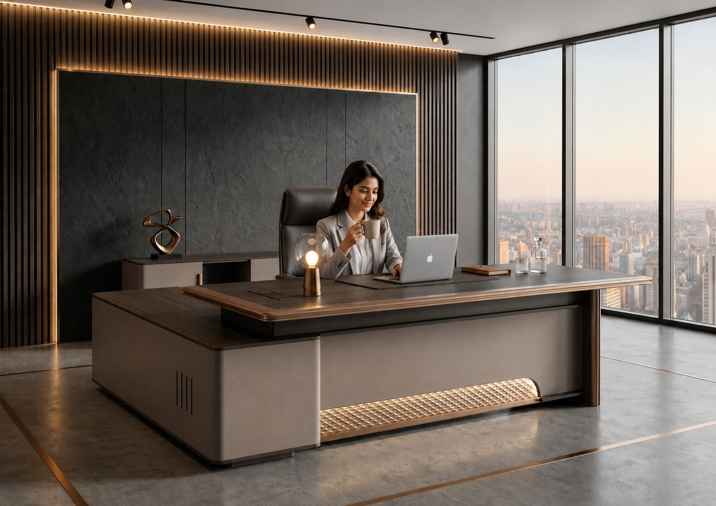 A woman sits at a large modern wooden desk in a high-rise office with floor-to-ceiling windows overlooking a city skyline. The desk has a dark wood top and a light taupe-gray base with integrated warm under-desk lighting.