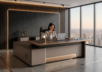 A woman sits at a large modern wooden desk in a high-rise office with floor-to-ceiling windows overlooking a city skyline. The desk has a dark wood top and a light taupe-gray base with integrated warm under-desk lighting.
