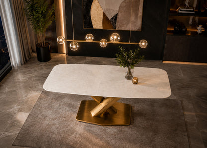 A modern rectangular dining table with a white marble-look top and a polished gold-tone geometric metal base, styled in a contemporary dining room setting.