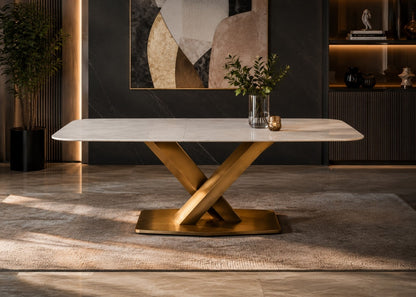 A modern rectangular dining table with a white marble-look top and a polished gold-tone X-shaped metal base, styled in a contemporary dining room setting.