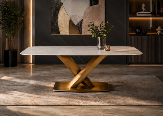 A modern rectangular dining table with a white marble-look top and a polished gold-tone X-shaped metal base, styled in a contemporary dining room setting.