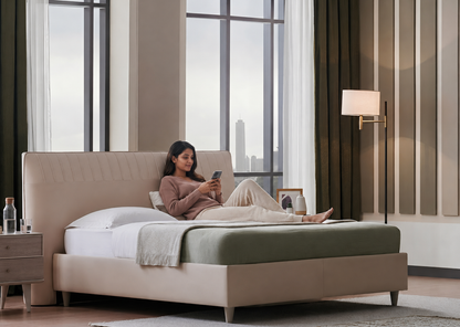 Woman lying on a bed in a modern bedroom with large windows and a cityscape view.
