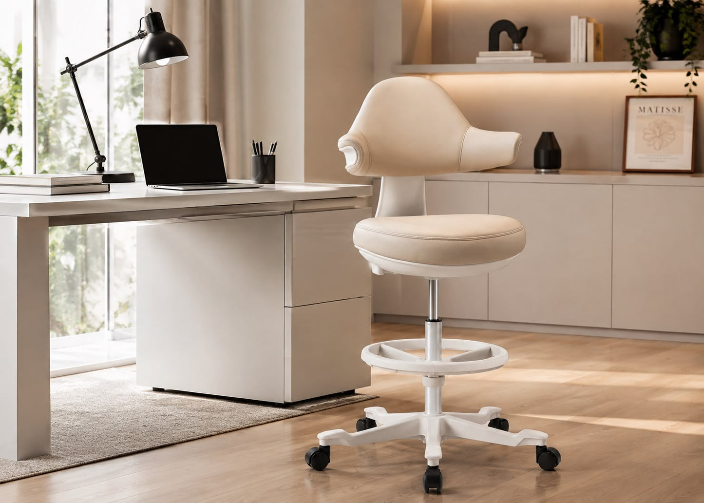 A cream-colored ergonomic office chair with a white wheeled base, positioned next to a matching cream desk in a modern, sunlit home office setting.