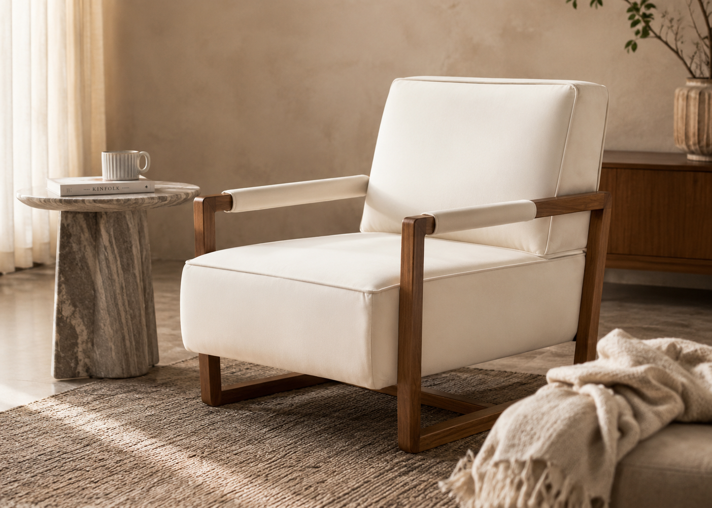 A modern accent chair with cream-colored upholstery and a medium brown wooden frame, styled in a warm, neutral-toned living room setting next to a marble side table.