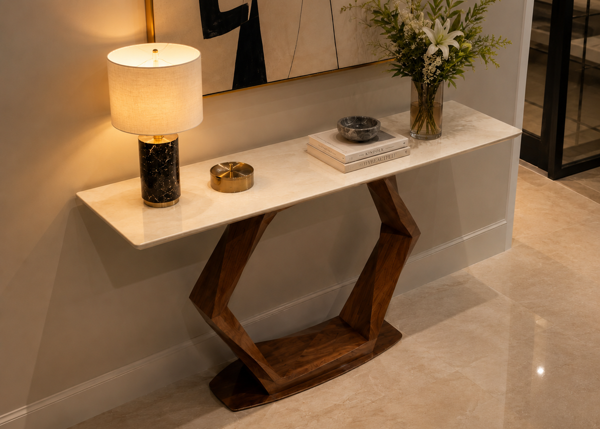 A modern console table with a white marble-look top and a sculptural dark wood geometric base, styled in a home interior with a table lamp, books, and a vase of flowers.