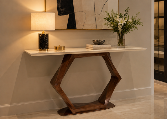 A modern hexagonal console table with a white marble top and dark brown wooden base, styled in a home entryway with a lamp, books, and a vase of flowers.
