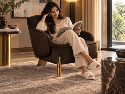 Varello Armchair with a woman reading in a relaxed luxury living room, showing the chair's generous scale and curved silhouette